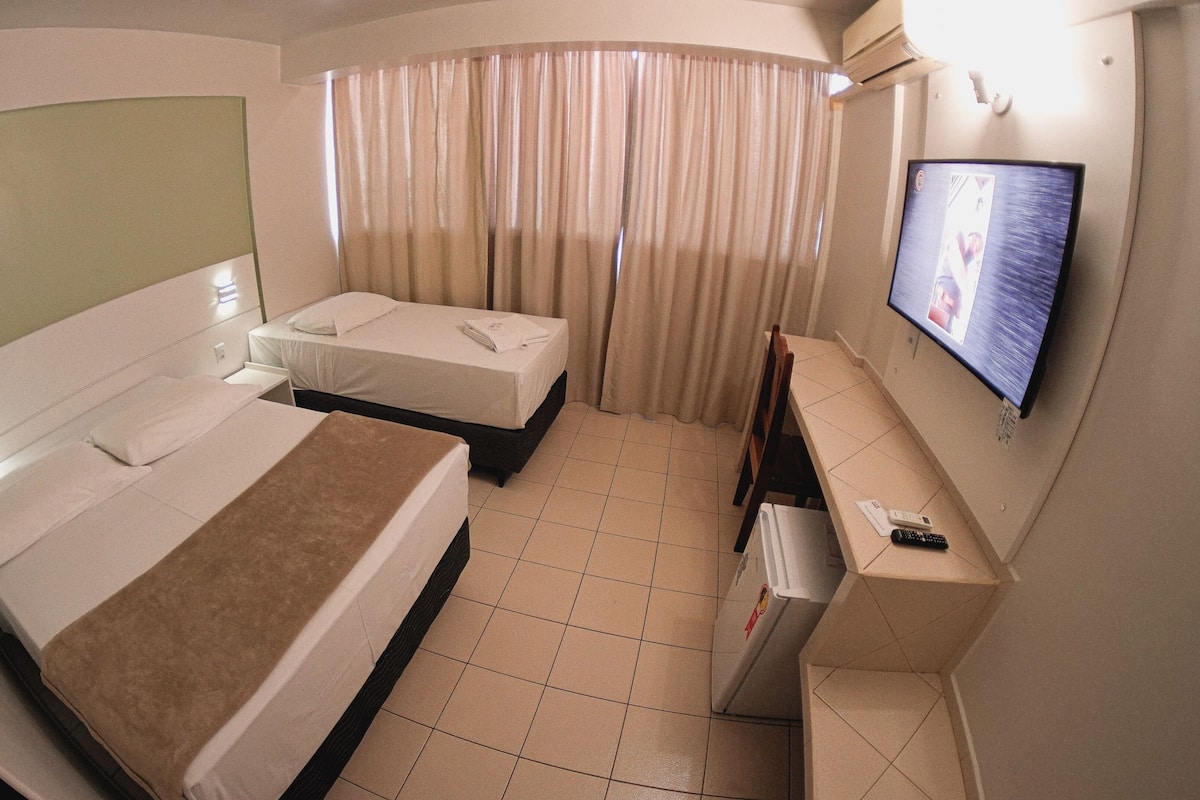 Ein Hotelzimmer mit zwei Betten, einem Fernseher, einem Schreibtisch und einem Stuhl.