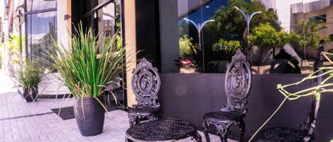 Outdoor seating with ornate metal chairs and a table, potted plants, and a building entrance.
