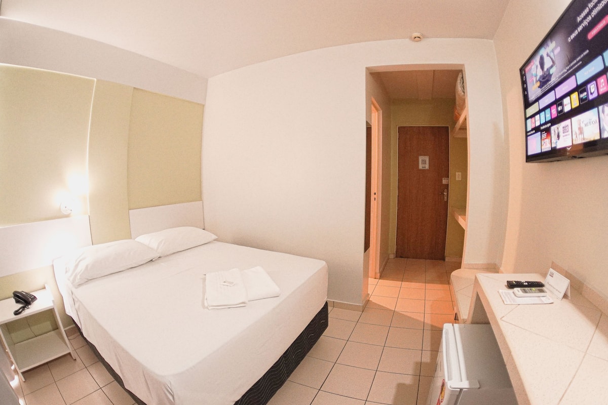 Ein Hotelzimmer mit Bett, Nachttisch, Fernseher und einer Tür zu einem weiteren Raum.