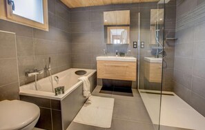 Moderni kylpyhuone, jossa on kylpyamme, wc, lasiseinäinen suihku ja peilillä varustettu pesuallas.