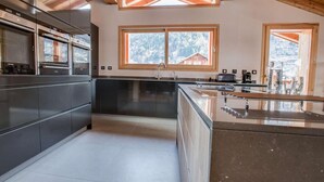 Une cuisine moderne dotée d’un îlot central, de grandes fenêtres et offrant une vue sur l’extérieur.