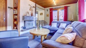 A cozy living room with a fireplace, a blue sofa, a wooden coffee table, and a bookshelf. - 1st floor, view ski slopes, balcony, fireplace or stove, parking, tv, 118m², Morzine (Morzine)