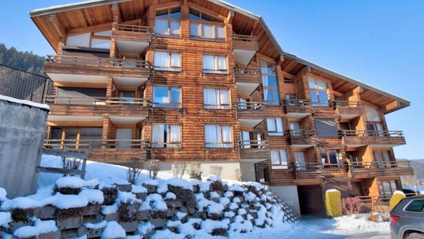 A multi-story wooden chalet with balconies, a stone retaining wall, and a snow-covered ground. - 50m from ski slopes, 2nd floor, view mountain, balcony, tv, ski locker, 38m², Morzine (Morzine)