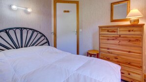 A bedroom with a bed, a wooden dresser, a small stool, a mirror, and a door with a light switch. - 50m from ski slopes, 2nd floor, view mountain, balcony, tv, ski locker, 38m², Morzine (Morzine)