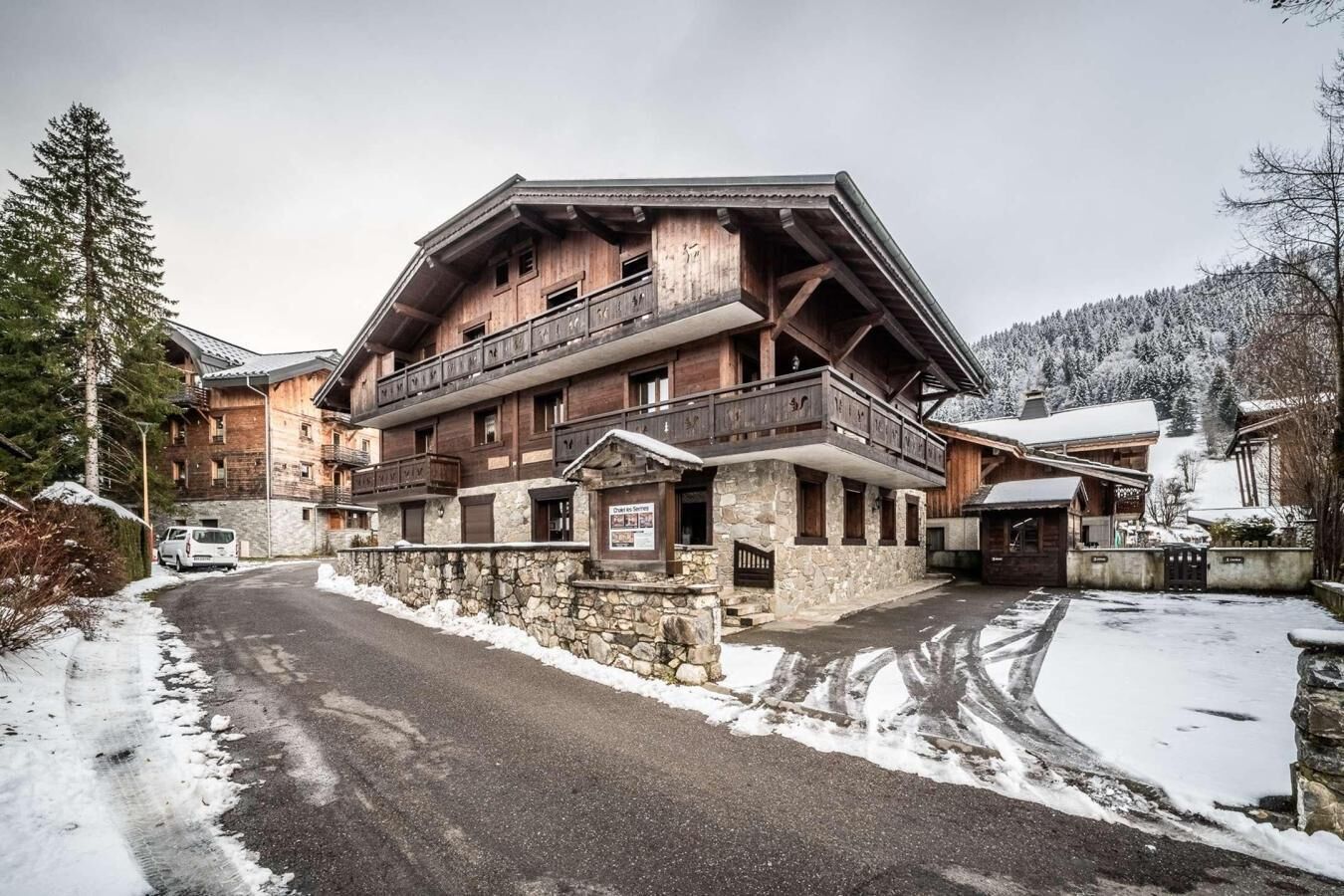 Un bâtiment en bois à plusieurs étages, doté de balcons, d’un mur en pierre et surplombant un paysage enneigé.