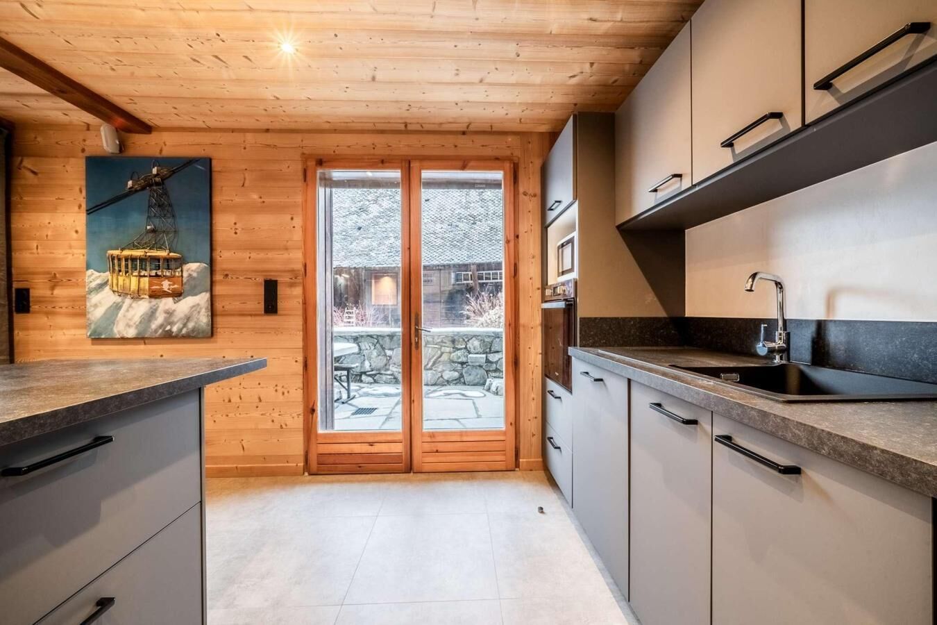 A modern kitchen with wooden walls, a large window, and a stone pathway leading outside.