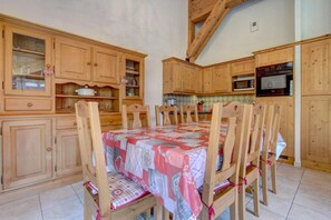 Een gezellige keuken met houten kastjes, een eettafel met stoelen en een magnetron.