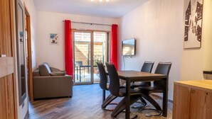 A modern room with a wooden floor, a sofa, a dining table with chairs, and a TV on the wall. - 100m from ski slopes, Ground floor, terrace, parking, tv, 31m², Morzine (Morzine)