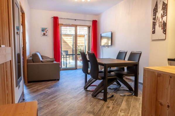 Ein modernes Zimmer mit Holzboden, einer Couch, einem Esstisch mit Stühlen und einem Fernseher an der Wand.