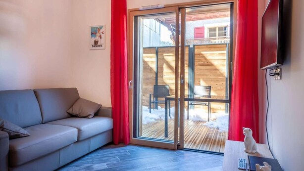 A room with a sofa, a table with a figurine, and a sliding glass door leading to an outdoor area with a wooden deck and a chair. - 100m from ski slopes, Ground floor, terrace, parking, tv, 31m², Morzine (Morzine)