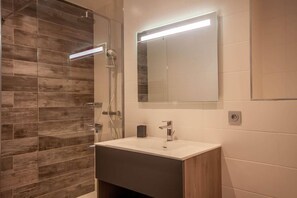 Ein modernes Badezimmer mit einer gläsernen Duschkabine, einem weißen Waschbecken mit dunklem Unterschrank und einem großen Spiegel darüber.