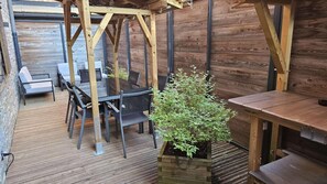 Eine Holzterrasse im Freien mit Tisch und Stühlen, umgeben von Holzwänden und einem Metallgeländer.