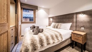 Een slaapkamer met een groot bed, een houten garderobe en een raam met uitzicht op gebouwen.