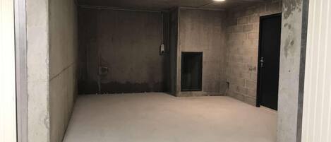 Un intérieur spacieux et brut, avec des murs en béton et un plancher plat, comprenant une porte et une petite fenêtre.