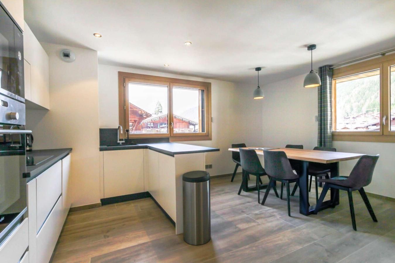 Una cocina moderna con comedor, suelo de madera y ventanas amplias.
