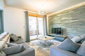 A modern living room with a sofa set, a coffee table, a flat-screen TV, and a stone-textured wall. - 100m from ski slopes, 1st floor, balcony, parking, tv, 86m², Morzine (Morzine)