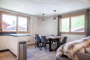 A modern kitchen with a dining area, large windows, and a dog on a couch. - 20m from resort center, 1st floor, balcony, parking, tv, 89m², Morzine (Morzine)