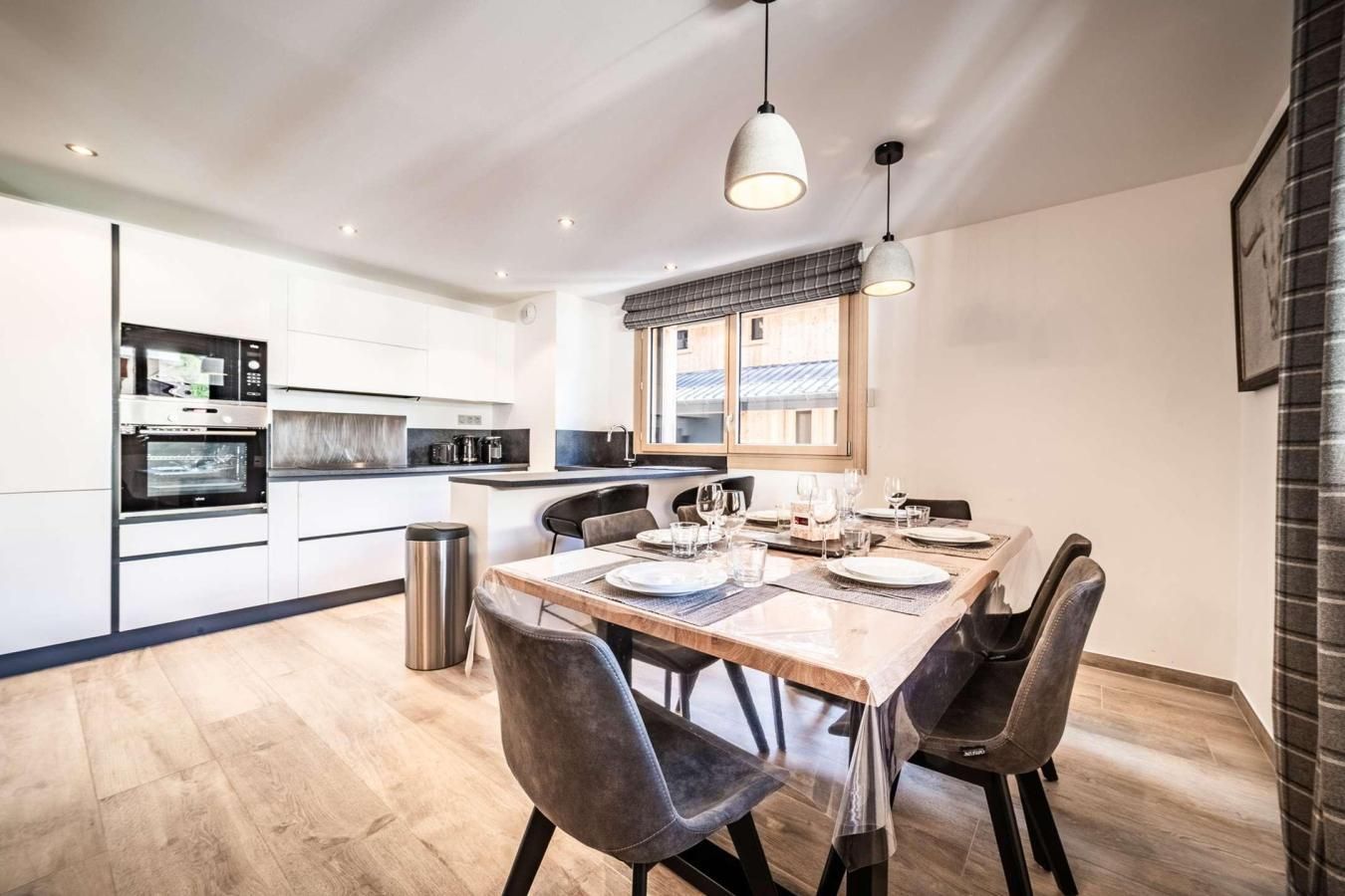 A modern kitchen with built-in appliances, a dining area with a wooden table and chairs, and a large window providing natural light.