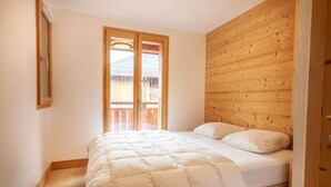 Un dormitorio con cabecera de madera, cama grande con ropa de cama blanca y puerta corrediza de vidrio que da a un balcón exterior.