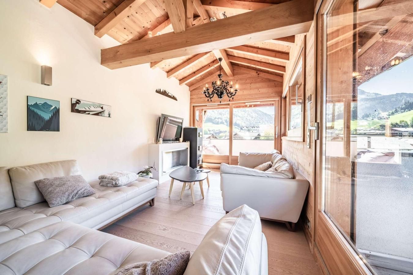 Una sala de estar moderna con techo alto, vigas de madera, una araña, un televisor y un sofá.