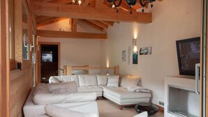 Una sala de estar moderna con un sofá seccional, un televisor de pantalla plana y vigas de madera en el techo.