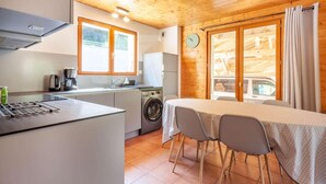 A compact kitchen with a washing machine, a dining table with chairs, and a large window with curtains. - Ground floor, view mountain, balcony, parking, tv, 64m², Morzine (Morzine)