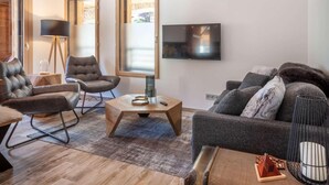 A modern living room with a sofa, two armchairs, a coffee table, and a TV.