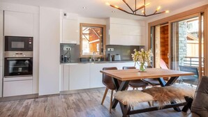 A modern kitchen with built-in appliances, a dining area with a wooden table and chairs, and a large window providing natural light.