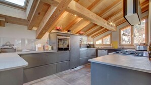 Une cuisine moderne dotée d’un îlot central, d’appareils électroménagers intégrés et d’un plafond en pente avec des poutres en bois.
