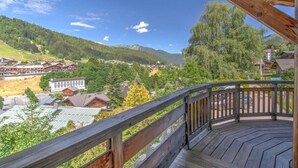 Une terrasse en bois offrant une vue sur un village et des montagnes.