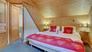 A bedroom with a wooden sloped ceiling, a bed with red heart-patterned bedding, two bedside lamps, and a wooden door. - 1st floor, view mountain, terrace, parking, tv, 160m², Morzine (Morzine)
