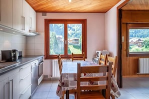 Une cuisine avec une table à manger, des chaises et une vue sur un paysage montagneux, visible à travers de grandes fenêtres.