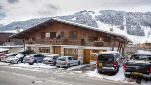Un edificio de madera con balcón, coches estacionados y una montaña nevada al fondo.