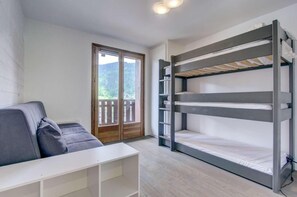 Una habitación con literas, un sofá, una mesita y un ventanal corredero que da a un espacio exterior.