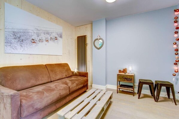 Una sala de estar acogedora con un sofá marrón, un banco de madera, una mesita auxiliar con una lámpara y una decoración con forma de corazón en la pared.