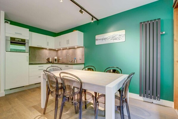 A modern kitchen with white cabinets, a dining table with chairs, and a green accent wall.