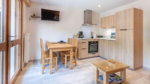Een moderne keuken met houten kastjes, een inbouwoven en een eethoek met een tafel en stoelen.