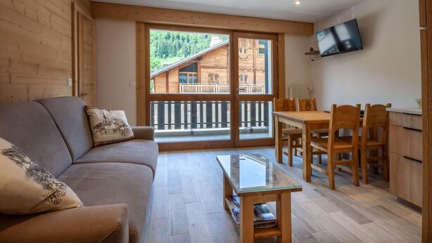 Een gezellige woonkamer met een bank, een glazen salontafel en een eethoek met houten stoelen en een tafel.