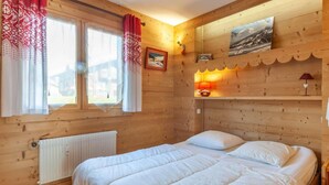 Ein Schlafzimmer einer Holzhütte mit einem Bett, einem Fenster mit Vorhängen, einem Heizkörper und Wandleuchten.