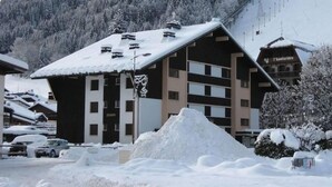 Ein Skiort-Gebäude mit mehreren Stockwerken, einem geneigten Dach und einem schneebedeckten Berg im Hintergrund.