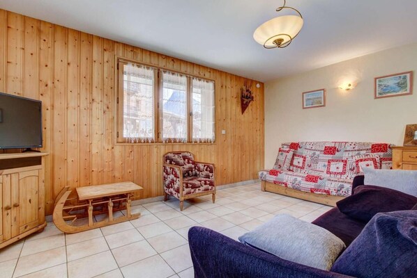 Une pièce aux murs lambrés, avec un canapé, un fauteuil à motifs, une table en bois et un téléviseur.