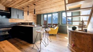 A modern kitchen with wooden ceiling, a central island, bar stools, and a view of mountains through large windows. - 50m from ski slopes, 3rd floor, view panoramic, swimming pool, sauna, hammam, balcony, tv (Champagny-en-Vanoise)