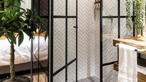A modern bathroom with a glass partition, a shower, a wooden vanity, and a potted plant.