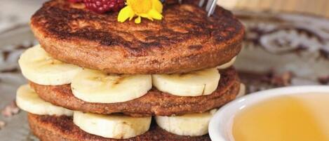 A stack of pancakes with bananas and berries, a flower, and a bowl of syrup.