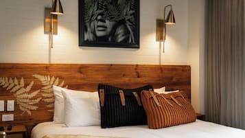 Un lit bien fait, avec une tête de lit en bois, deux lampes fixées au mur et une œuvre d’art encadrée au-dessus.