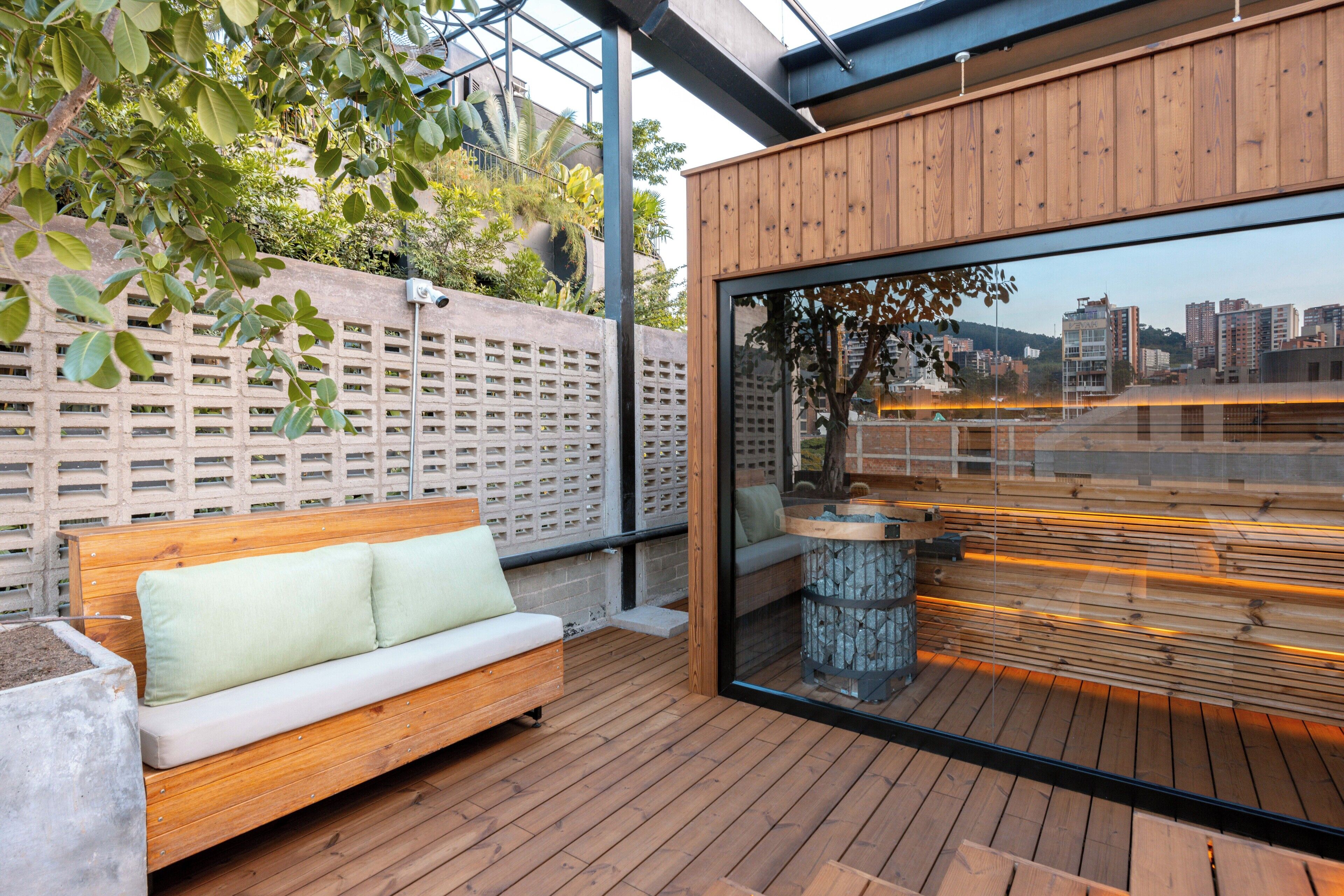 Terraza de madera con banco y pared de vidrio que ofrece vista a la ciudad.