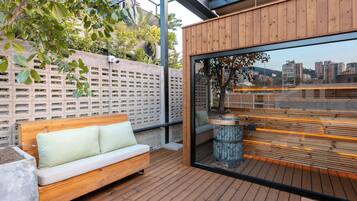 Terraza de madera con banco y pared de vidrio que ofrece vista a la ciudad.