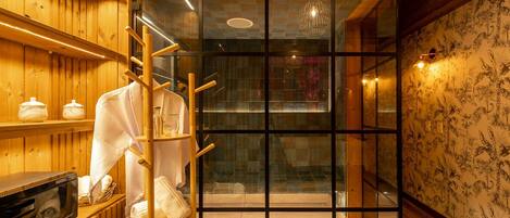 A modern bathroom with wooden walls, a glass shower enclosure, and a towel rack with towels.