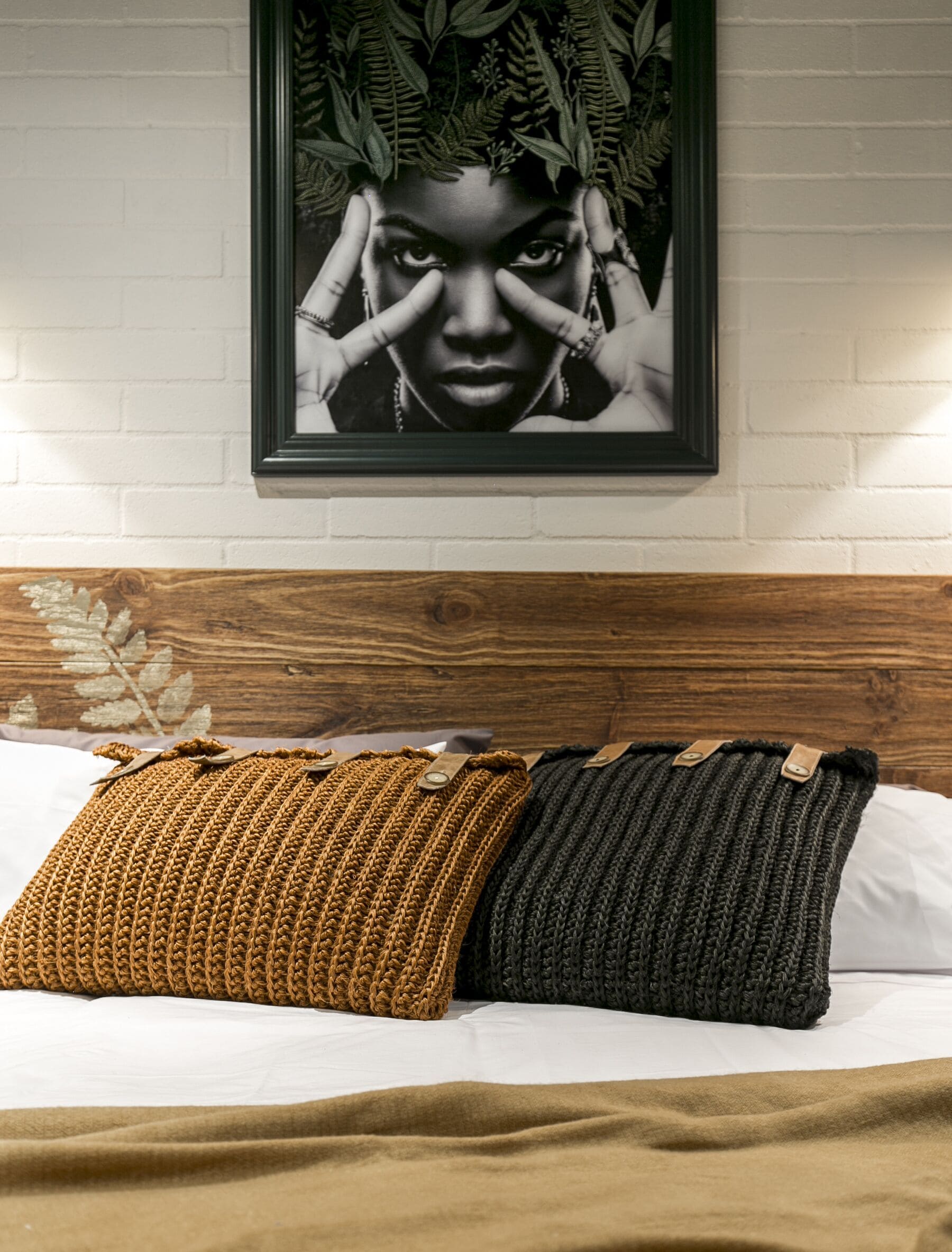 Un letto con due cuscini lavorati a maglia, una testiera in legno e un quadro appeso alla parete.