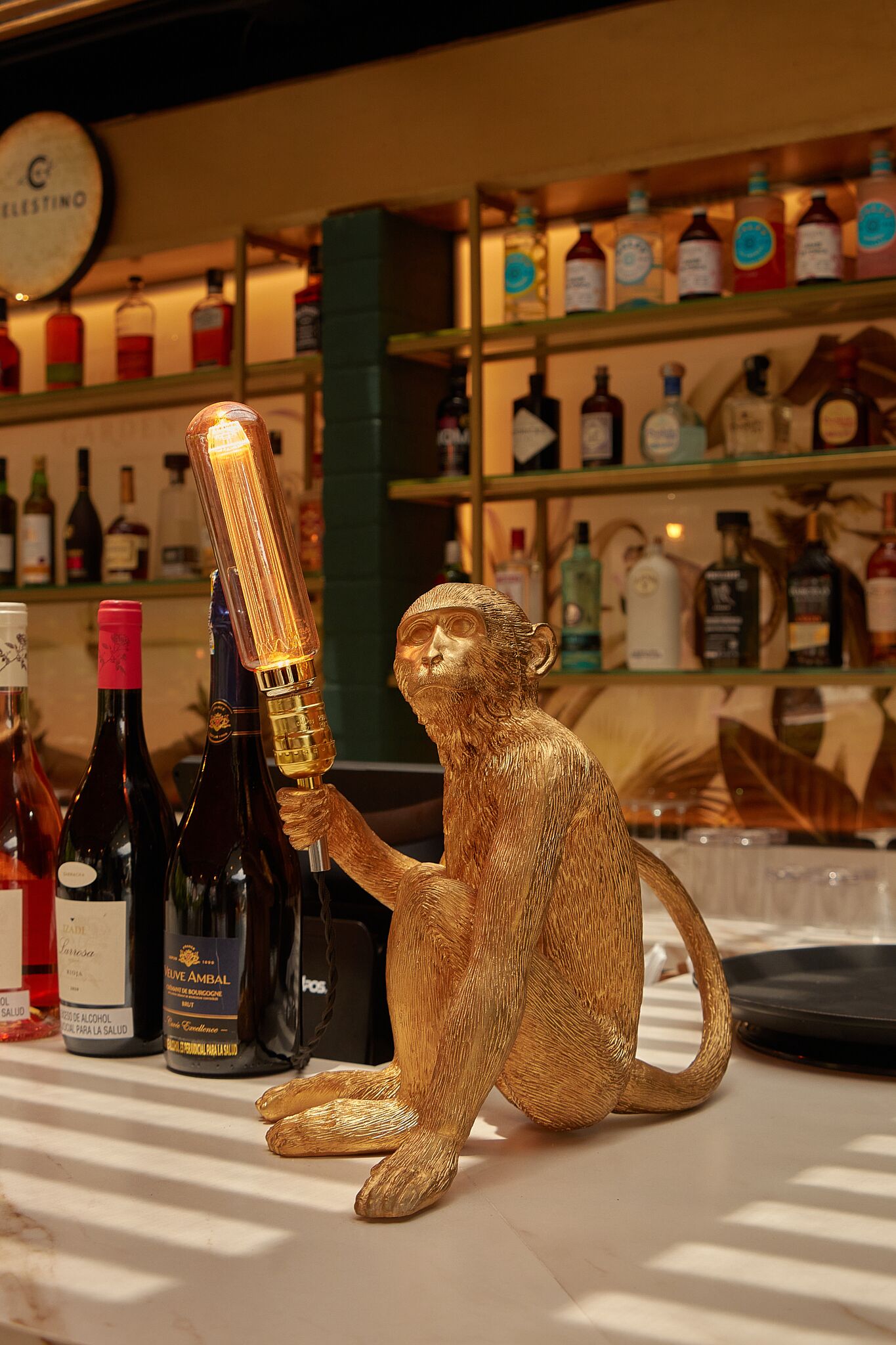 A gold monkey sculpture holding a bottle, surrounded by various liquor bottles on shelves.
